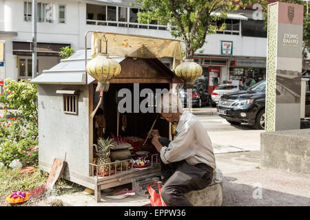 Un homme s'allume de l'encens dans un petit côté route de culte dans la région de Tiong Bahru Singapour. Banque D'Images