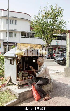 Un homme s'allume de l'encens dans un petit côté route de culte dans la région de Tiong Bahru Singapour. Banque D'Images