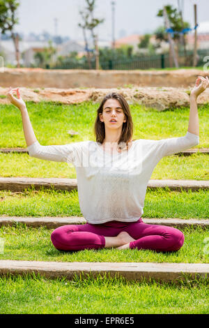 Jeune femme makinYoung femme faisant ses exercices de yoga dans le parc sur le stairsg Le Yoga dans le parc autorisation Modèle disponible Banque D'Images