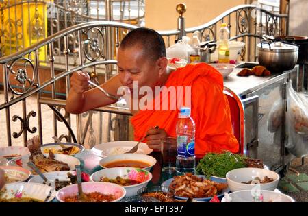 Bangkok, Thaïlande : Le moine bouddhiste dans une robe orange manger un somptueux déjeuner sur une terrasse extérieure au Wat Hua Lamphong Banque D'Images