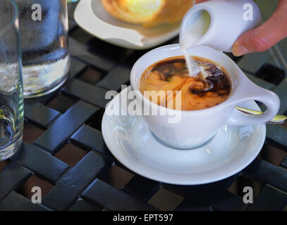On verse la crème dans le café dans la tasse et soucoupe blanc sur l'extérieur, table patio, Canada Banque D'Images