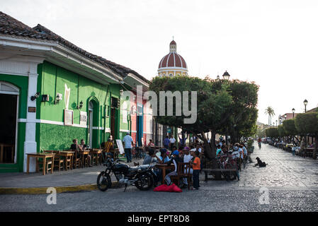 Restaurants et Cathédrale de la Calle la Calzada Grenade Nicaragua // GRENADE, Nicaragua — Calle la Calzada, une importante artère piétonne de Grenade, s'étend du Parque Central jusqu'aux rives du lac Nicaragua. Cette rue historique est l'un des principaux centres commerciaux et sociaux de la ville coloniale, bordée de restaurants, bars et boutiques logés dans des bâtiments colorés restaurés. Le dôme jaune distinctif de la cathédrale de Grenade, officiellement connue sous le nom de cathédrale de l'Assomption de Marie, est visible au loin. Calle la Calzada dispose de divers monuments et est k Banque D'Images