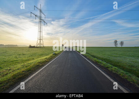 Route de campagne avec l'électricité pylône dans matin avec Soleil, Freiensteinau, Vogelsbergkreis, Hesse, Allemagne Banque D'Images
