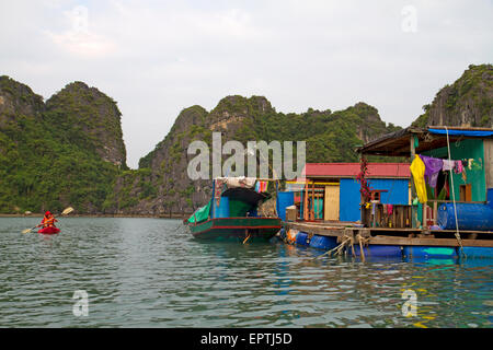 Kayak passé un village de pêcheurs flottant dans la baie d'Halong Banque D'Images