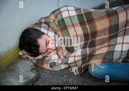 Jeune homme mendiant dormant sur les trottoirs de la ville d'une couverture sur ses épaules Banque D'Images