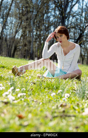 Belle femme assise dans l'herbe entouré de marguerites de printemps Banque D'Images