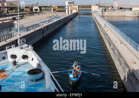 Bateau à rames d'un équipage de la population locale la vente de cadeaux touristiques entre dans l'écluse à Esna sous la proue d'un navire de croisière du Nil, l'Egypte Banque D'Images