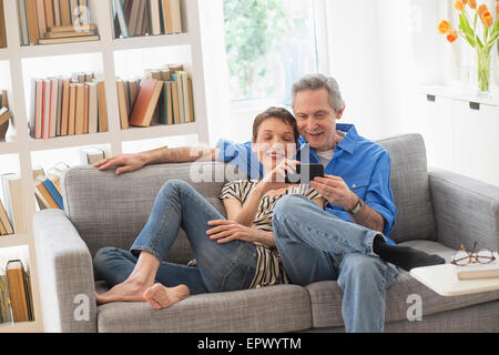 Partage Senior couple cell phone on sofa Banque D'Images