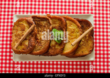 Torrijas espagnol avec la cannelle et la menthe poivrée sur un plat blanc sur une nappe blanche et rouge Banque D'Images