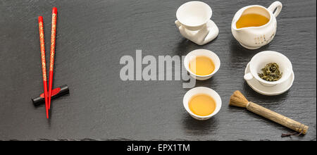 La table pour la cérémonie du thé traditionnelle asiatique. Théière, tasses et baguettes rouge sur fond noir Banque D'Images