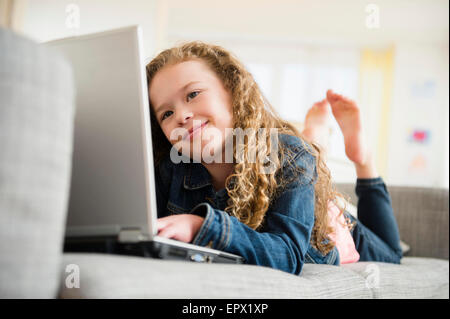 Girl (10-11) avec laptop lying on sofa Banque D'Images