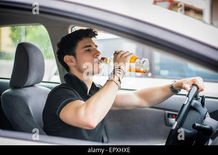Beau jeune homme au volant de sa voiture alors que la consommation d'alcool dans le trafic Banque D'Images