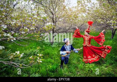 Danse femme kazakh en robe rouge et l'homme jouant de la dombra au printemps jardin à Almaty, Kazakhstan, en Asie centrale Banque D'Images