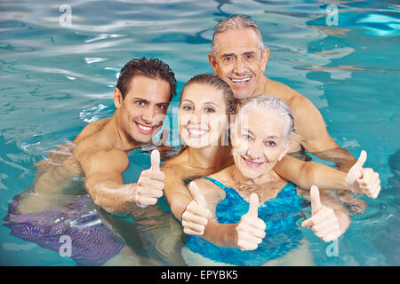 Famille heureuse avec senior couple in swimming pool holding Thumbs up Banque D'Images