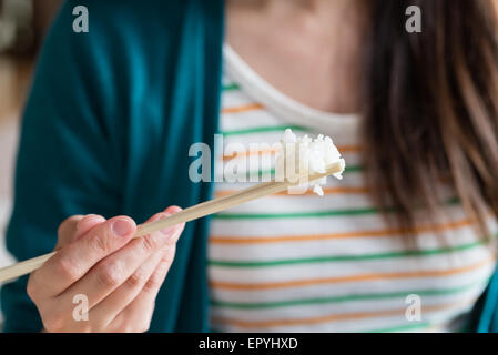 Un gros plan d'une jeune fille manger du riz avec des baguettes en bois. Banque D'Images