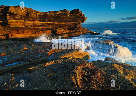 Seascape Sunrise orange avec des rochers et des piscines extérieures de l'océan et les coquillages avec ciel nuageux ciel d'orage et falaises lointaines Banque D'Images