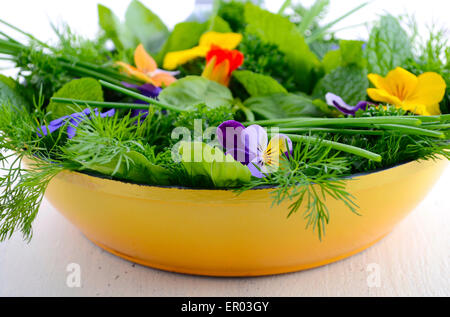 La cuisson avec des herbes concept avec fines herbes et fleurs comestibles dans la poêle à frire d'moderne jaune sur la table de bois blanc. Banque D'Images