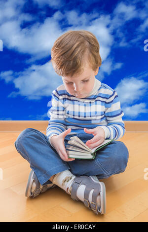 Boy reading book coin sur le sol et ciel nuages en arrière-plan Banque D'Images