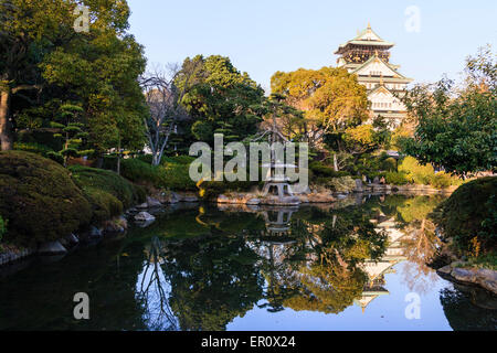Donjon du château d'Osaka, style borogata, dominant le jardin japonais du palais de Kishu et se reflétant dans l'étang. Lanterne en pierre au premier plan. Banque D'Images