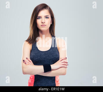 Jeune femme fitness en vêtements sports debout avec les bras croisés sur fond gris et looking at camera Banque D'Images