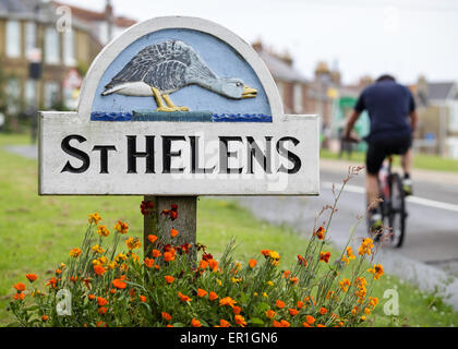 Un cycliste, équitation passé le panneau du village de St Helens (AKA Goose Island) à côté du vert sur l'île de Wight. Banque D'Images