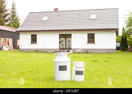 Des bidons de lait devant une maison, village rural arrière-plan. Banque D'Images