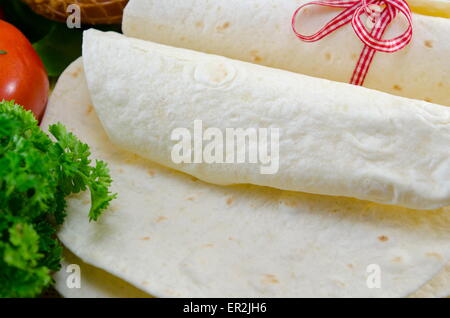 Tortillas vides attachées avec un ruban rouge sur une table avec tomate, salade et jambon Banque D'Images