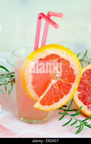 Jus de pamplemousse frais dans un verre décoré d'une tranche de pamplemousse rouge sur une table décorée avec Rosemary branch Banque D'Images