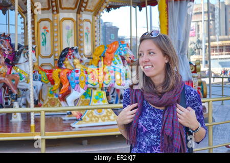 Happy girl se trouve en face d'un carrousel dans un amusement park Banque D'Images