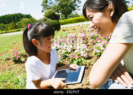 Mère et fille japonaise avec le comprimé dans un parc de la ville Banque D'Images