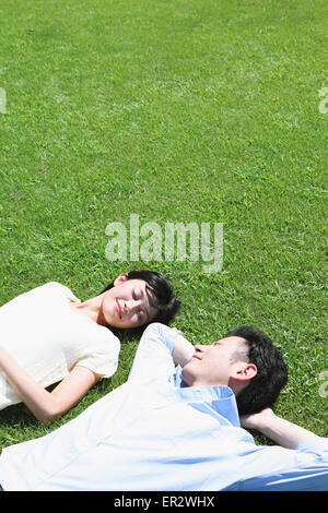 Heureux couple japonais portant sur l'herbe dans un parc Banque D'Images