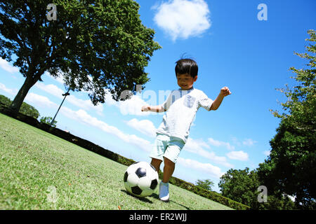 Jeune garçon japonais joue au soccer dans un parc de la ville Banque D'Images