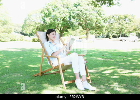 Femme japonaise avec tablette sur une chaise dans un parc de la ville Banque D'Images