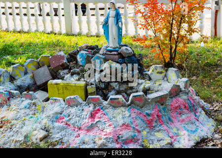 Statue de la Vierge Marie parmi les arbres d'érable. Mauvaises herbes vertes et peint en gris couleur des pierres dans un jardin de Medjugorje Banque D'Images