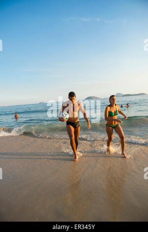 RIO DE JANEIRO, Brésil - 1 avril 2014 : Jeune homme et femme brésilienne à pied avec le football sur la rive de la plage d'Ipanema posto 9. Banque D'Images