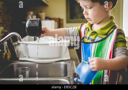 Garçon jouant avec les tasses à mesurer et de l'eau dans l'évier Banque D'Images