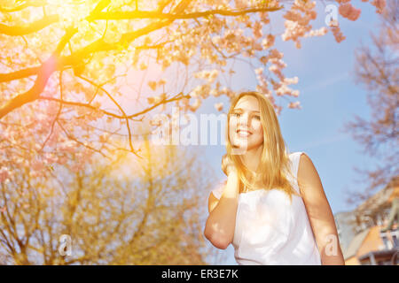 Jeune blonde woman standing on journée ensoleillée sous cherry tree in spring Banque D'Images