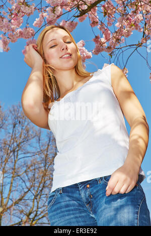 Jeune femme blonde en vertu de blooming Cherry Tree à partir de ci-dessous Banque D'Images