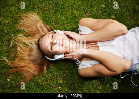 Jeune femme d'écouter de la musique avec un casque portant sur un pré en été Banque D'Images