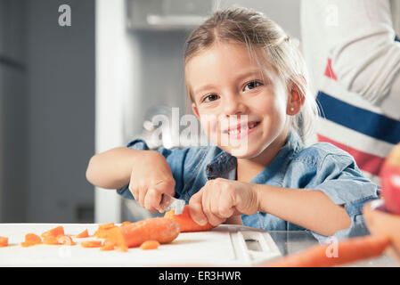 Petite fille de trancher les carottes en cuisine, portrait Banque D'Images