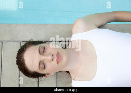 Jeune femme au soleil au bord de piscine avec les yeux fermés, overhead view Banque D'Images