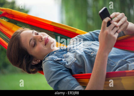 Woman relaxing in hammock with smartphone Banque D'Images