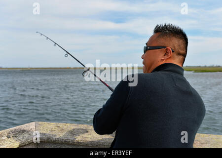 Merrick du sud, New York, USA. 24 mai 2015. Le révérend David YI, de Douglaston, Queens, est la pêche dans la baie de Merrick de l'embarcadère de Levy Park & préserver pendant le week-end du Memorial Day. Le groupe du pasteur est allé au parc parce qu'ils ne pouvaient pas aller à Jones Beach pour les poissons, pour les promenades de la région ont été fermées après la plage remplie à pleine capacité pour le Bethpage New York Air Show, qui pourrait être vu plus tôt d'une distance dans le ciel derrière lui. Banque D'Images