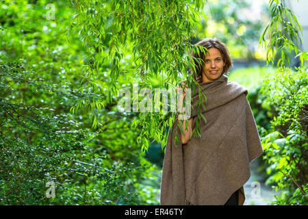 Jeune femme charmante dans le parc parmi le vert des arbres. Banque D'Images