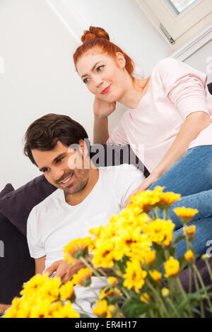 Jeune couple en appui sur le canapé dans le salon tandis que l'homme est de regarder la télévision et d'une femme est en train de lire un livre. Banque D'Images