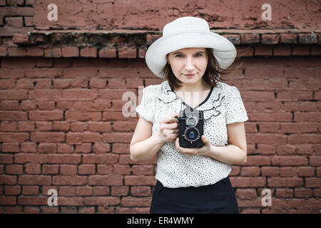 Femme photographe en white hat avec ancienne rétro caméra sur un background vintage brown mur de briques. Selective focus sur le modèle. Na Banque D'Images