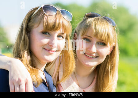 Jolies filles jumelles s'amuser au parc d'été en plein air. Jeune femme souriante avec des lunettes à la caméra en