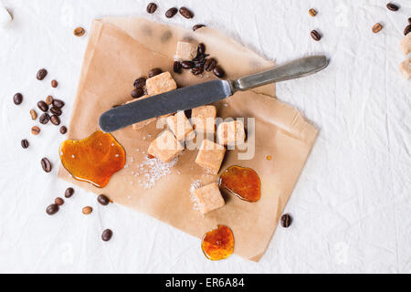 Bonbon caramel, les grains de café et de caramel sur du papier sulfurisé, a servi plus de nappe blanche avec couteau vintage Banque D'Images