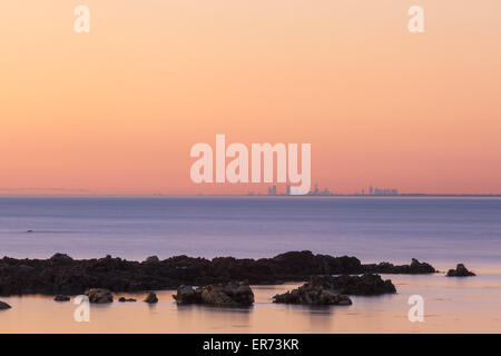 Melbourne CBD skyline at sunset dans la distance avec des rochers au premier plan. Banque D'Images