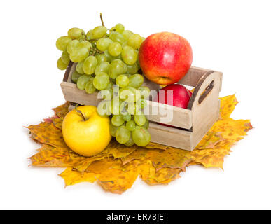 Des pommes et du raisin dans la caisse sur les feuilles d'automne background Banque D'Images